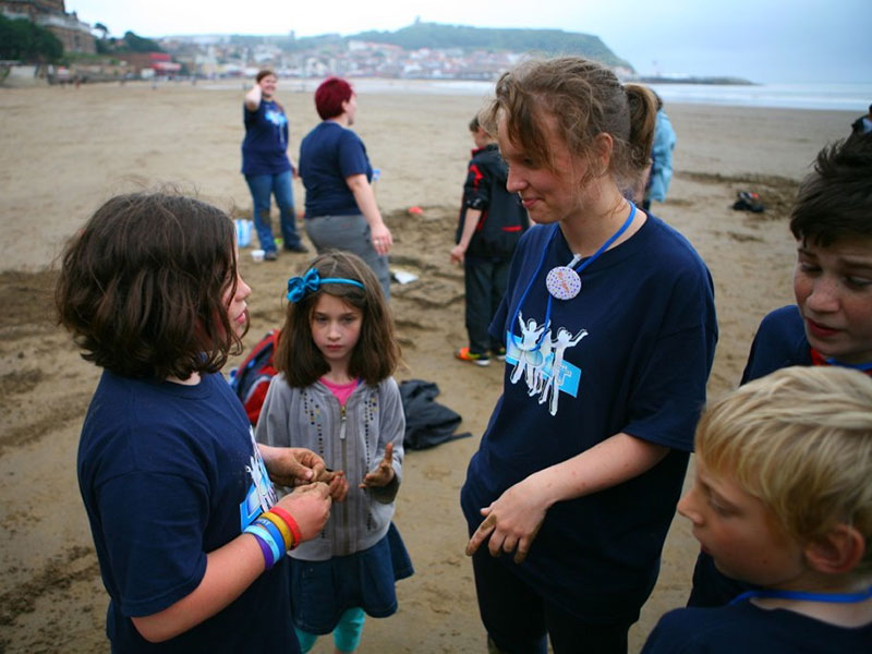 A group of adults, young people and children stood on a beach