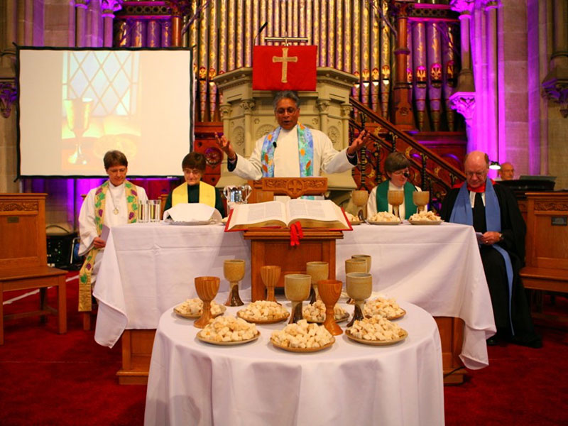 Minister stood at an altar leading worship. Four other ministers are sat at the altar either side