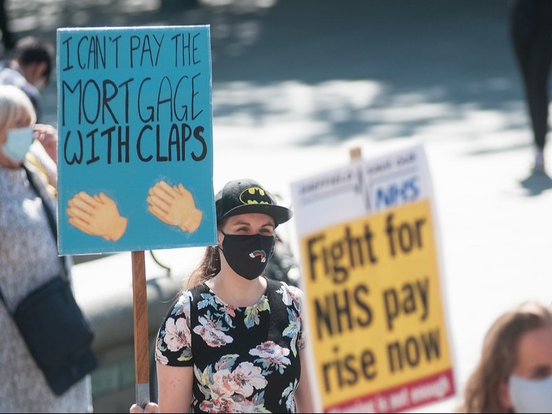 NHS staff pn a protest march carrying placards - one placard has 'I can't pay the mortgage with claps' and the other one says 'Fight for NHS pay rise now'
