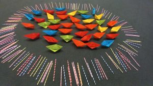 Multi-coloured origami boats gathered and circled by multicoloured straws, used as a resource for prayers