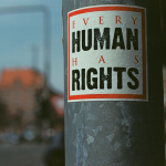 A lampost with a white sticker with a red border, inside of which says "Every human has rights".