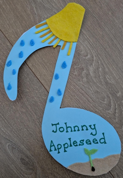 Cutout musical note with stuck-on felt sun, raindrops, earth and seedling. Text reads Johnny Appleseed.
