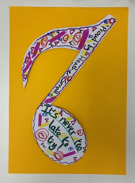 The reverse of a musical note made from paper. The colourful design has text written along it: It's never too late to try. "Proud" by Heather Small.